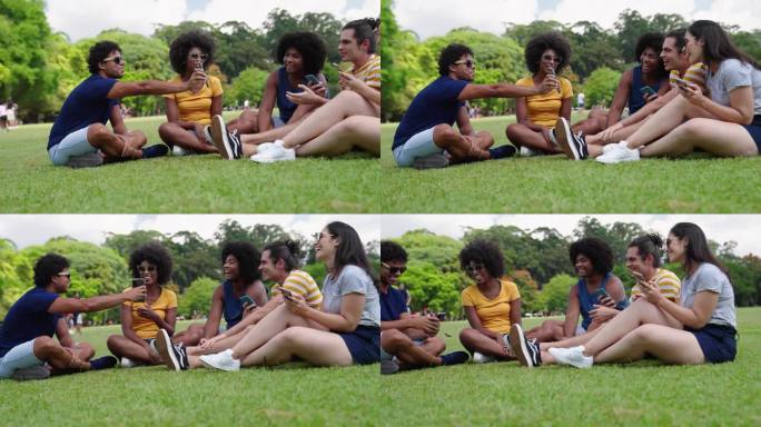 一群多民族青年朋友坐在公园里有说有笑。形形色色的朋友在智能手机上看搞笑视频