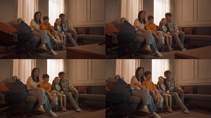 幸福的韩国家庭:妈妈和爸爸在沙发上看着有趣的家庭电视节目，和他们的小儿子和女儿一起笑。兄弟姐妹和父母