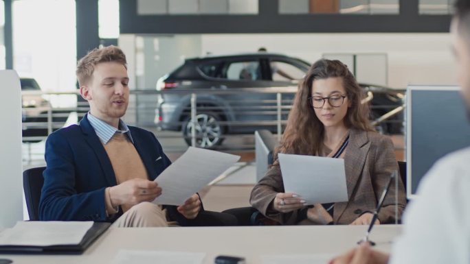 年轻夫妇在汽车经销店阅读汽车销售合同条款
