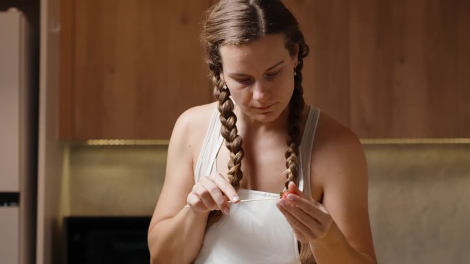 一个扎着辫子、系着白围裙的年轻女子正在厨房里把草莓串在串串上。