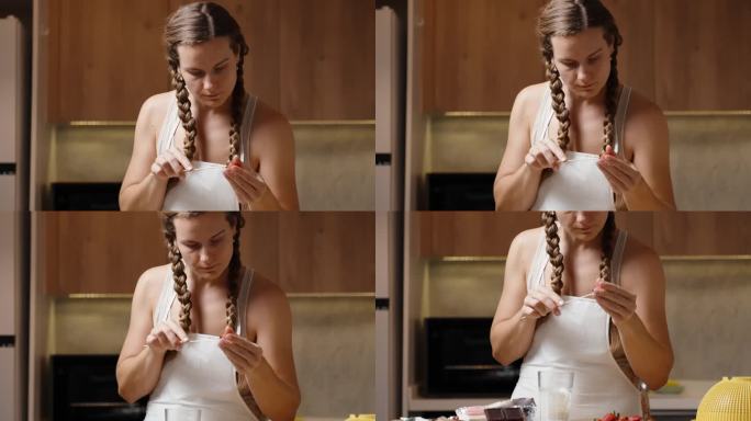 一个扎着辫子、系着白围裙的年轻女子正在厨房里把草莓串在串串上。
