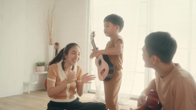 通过音乐建立快乐的亚洲家庭:父母和儿子在家里弹吉他。