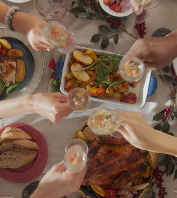 垂直画面:家人和朋友聚在家里吃传统的圣诞晚餐，烤火鸡盛宴。从上往下看，人们举起香槟酒杯，举杯庆祝
