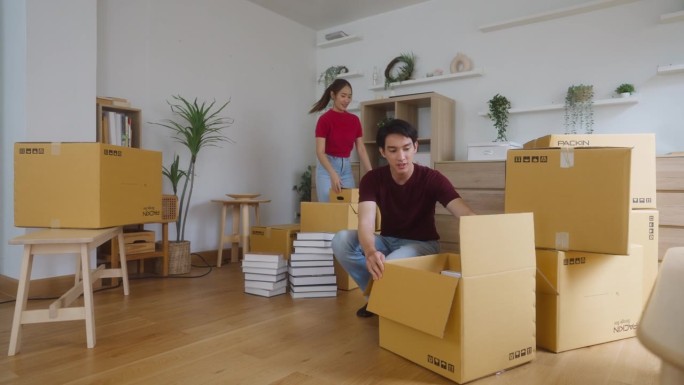 一对年轻的夫妇在他们的第一所房子里组建了家庭，他们微笑着互相帮助，拿起搬家用的纸板箱，把几个盒子放在