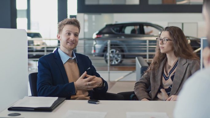 年轻的白人夫妇在签订合同后与汽车推销员聊天