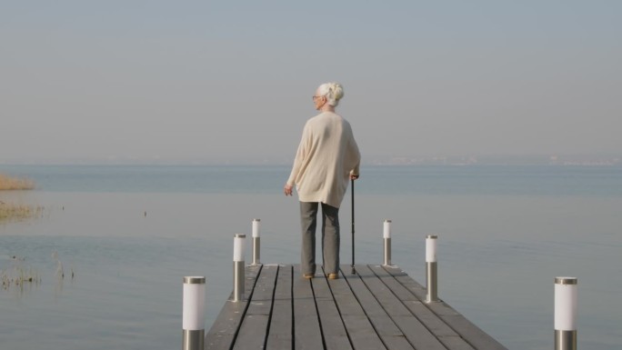 老妇人站在木码头上看湖