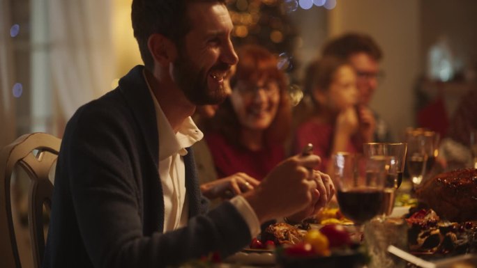 老人和年轻的男人和女人坐在一起在一个舒适的圣诞晚餐庆祝在家里的肖像。每个人都面带微笑，在装饰精美的客