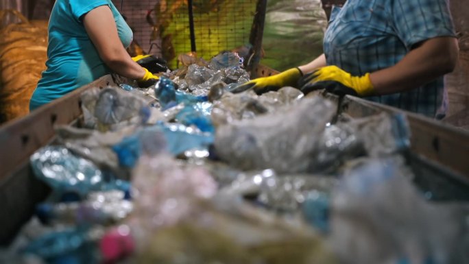 在垃圾回收厂，穿着特殊服装的工人在传送带上对塑料垃圾进行分类