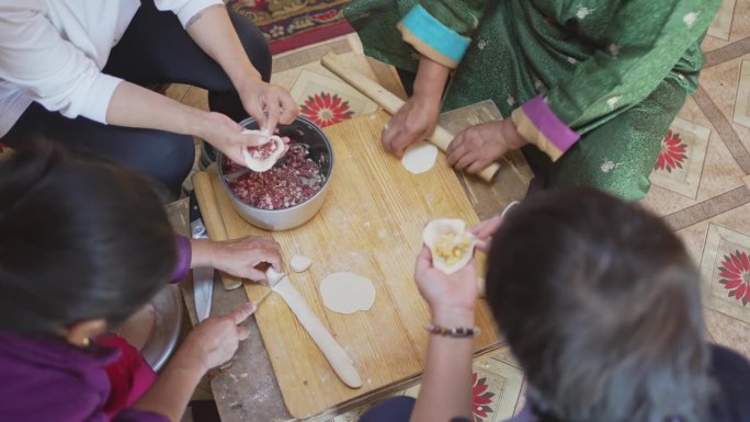 亚洲中国女游客学习制作蒙古传统饺子布兹与当地蒙古妇女在蒙古包里揉捏