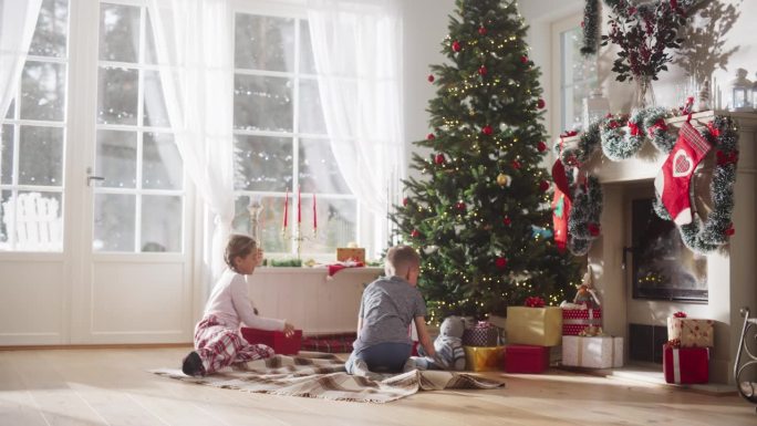 可爱的孩子们迫不及待地从家里的圣诞树下拿礼物的慢动作。快乐的小男孩和小女孩在节日早晨醒来收到新玩具