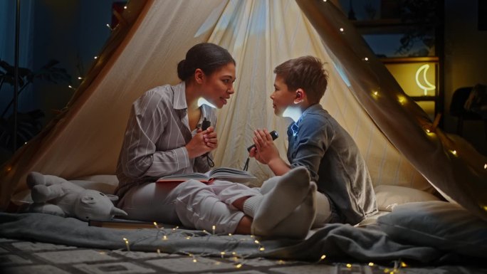 母亲和儿子拿着手电筒读睡前故事，在游戏帐篷里讲恐怖故事