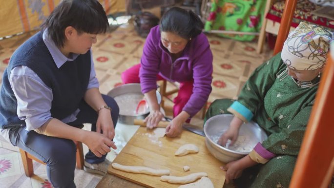 亚洲中国女游客学习制作蒙古传统饺子布兹与当地蒙古妇女在蒙古包里揉捏