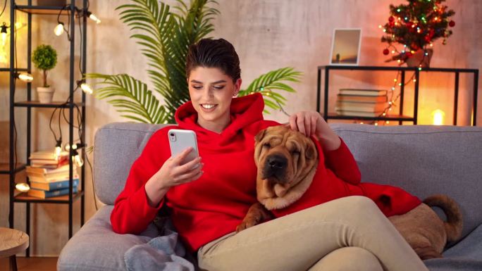 平安夜，一名年轻女子和她的狗坐在家里玩手机