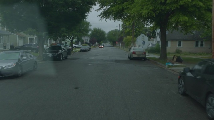 多佛尔住宅区正在下雨。汽车停在树下避雨。驾驶板，道路视角，挡风玻璃照明弹