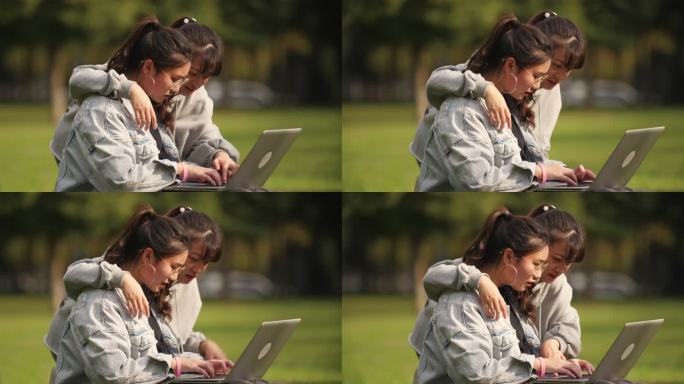 两位女大学生坐在校园草地上用电脑讨论学习