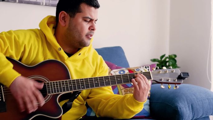 一名身穿黄色毛衣的哥伦比亚男子在舒适的客厅里弹着吉他
