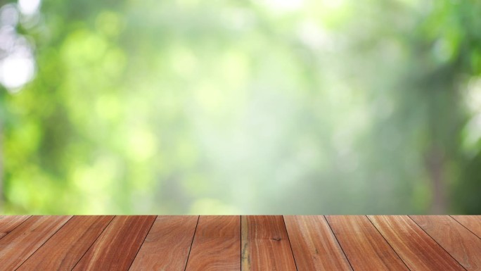 夏日的木桌吧台，与大自然背景绿树的散景模糊动画和阳光。