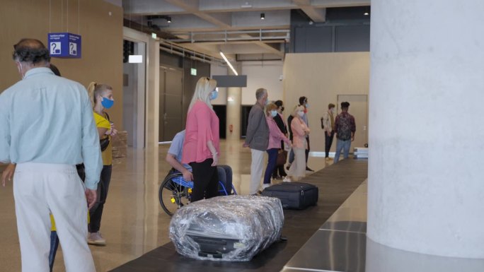 在新冠肺炎疫情期间，多种族乘客在机场行李传送带前排队等候行李