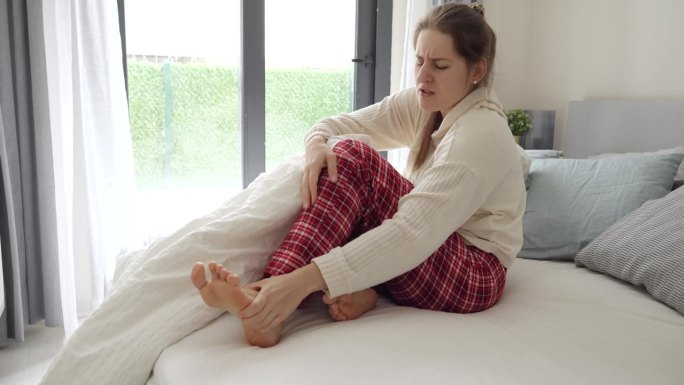 年轻女子感觉腿抽筋躺在床上按摩脚。伤害的概念，健康问题，疼痛和创伤