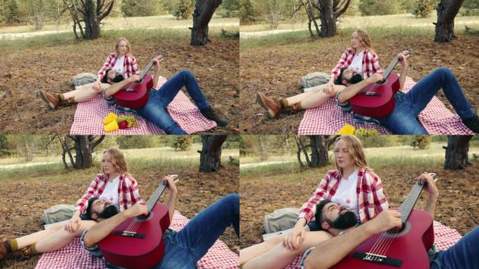 热恋的年轻夫妇，男人和女人在温暖的阳光下在森林里野餐。一个男人为他漂亮的女朋友弹吉他