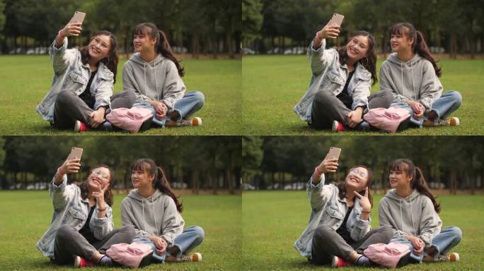 两位开心的女大学生坐在校园草坪上手机自拍