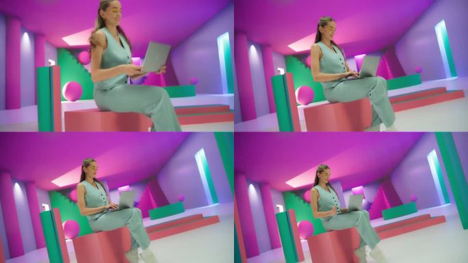 穿着鲜艳衣服的年轻女子坐在几何抽象的环境中使用笔记本电脑。富有创造力的年轻女性在色彩缤纷的工作室里愉