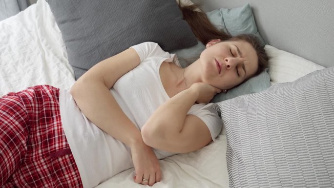 年轻女子睡在不舒服的枕头和床垫上后颈部疼痛。医疗保健问题，疼痛缓解和伤害的概念