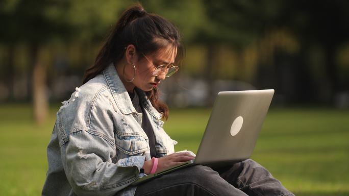 一位女大学生坐在校园草地上用笔记本电脑