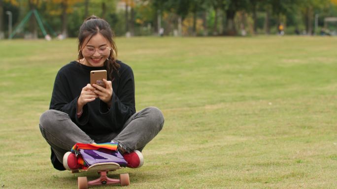 女大学生在大学校园草坪上快乐玩手机上网