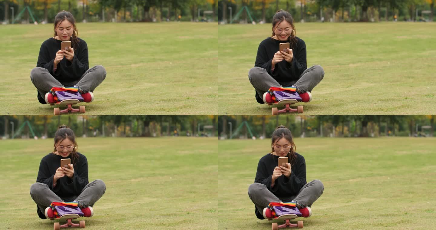 女大学生在大学校园草坪上快乐玩手机上网