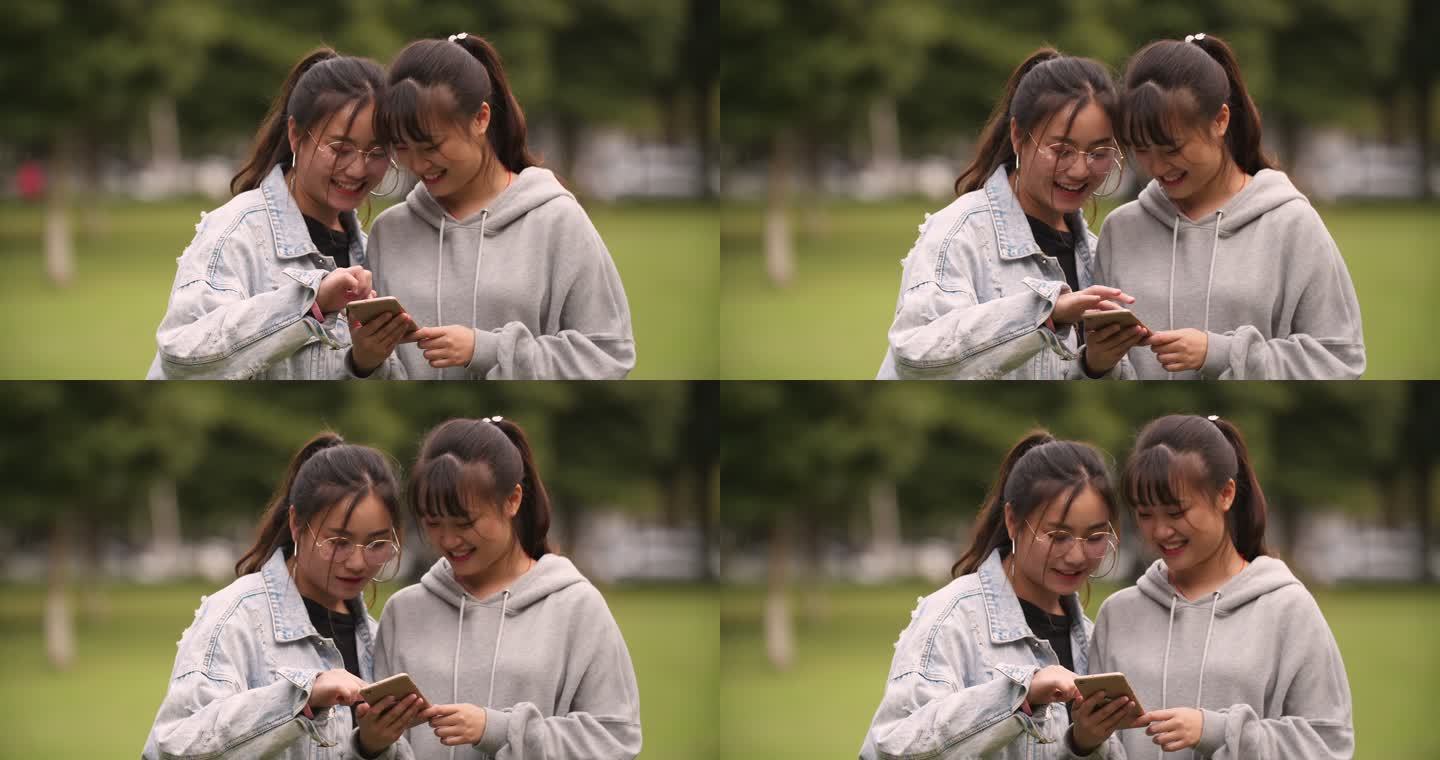 两位女大学生坐在校园草地上看手机聊天