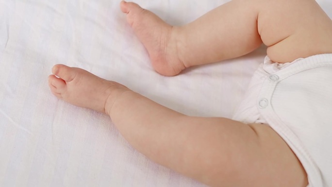 在一张白色的隔离照片中，一个新生婴儿的腿躺在床上，婴儿的脚跟特写在焦点上