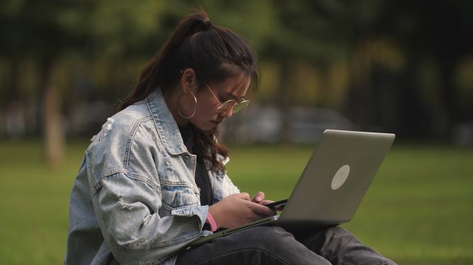 一位女大学生坐在校园草地上用笔记本电脑