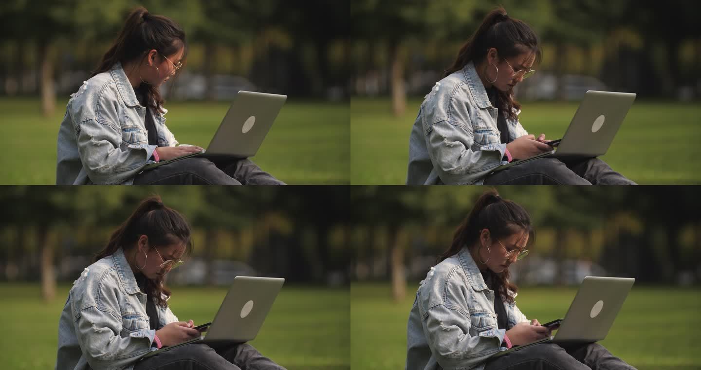 一位女大学生坐在校园草地上用笔记本电脑