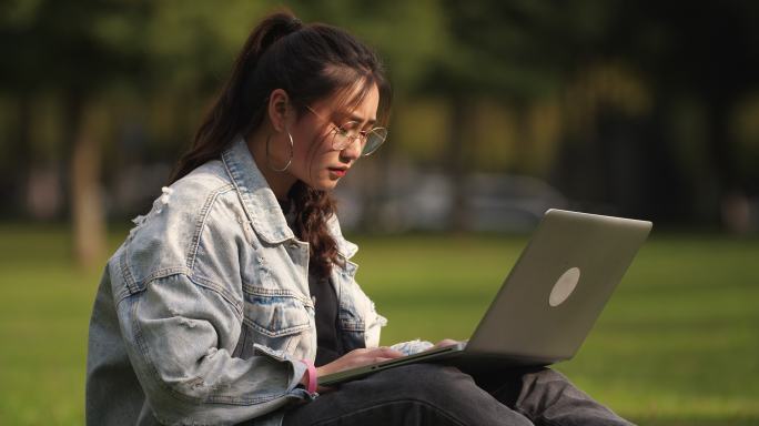 女大学生在大学校园里草地上用电脑学习
