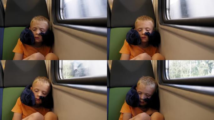 一个抱着颈枕的小男孩坐在火车上靠窗的地方睡觉。