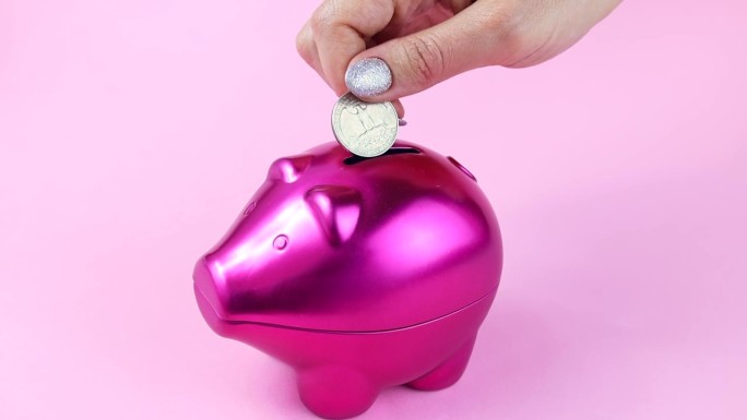 亮粉色的猪钱箱和手掉硬币在浅粉色的背景。经济，预算和节约的概念