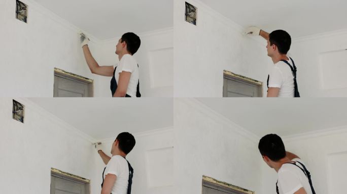 穿制服的修理工用刷子把墙壁刷成白色