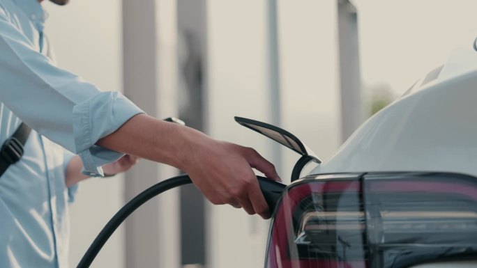 环保生活方式:亚洲男子用绿色科技为他的电动汽车充电。
