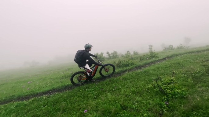 男子极限自行车骑在山路上的细径绿草与雾雾鸟瞰