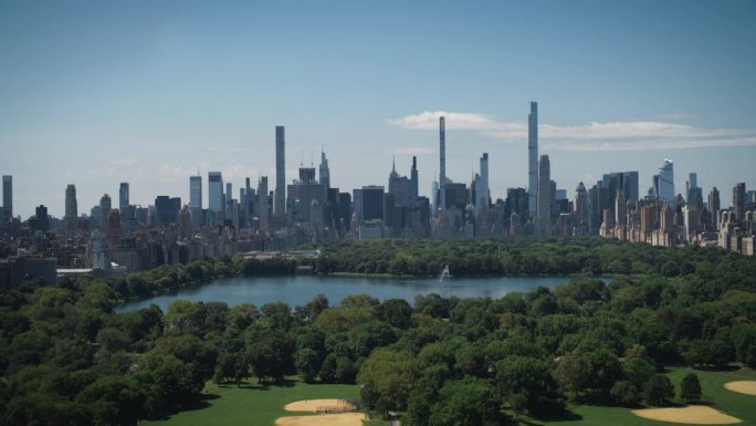 空中直升机镜头在中央公园与自然，树木，人们野餐和休息在曼哈顿摩天大楼周围的田野景观。美丽的晴天。慢动