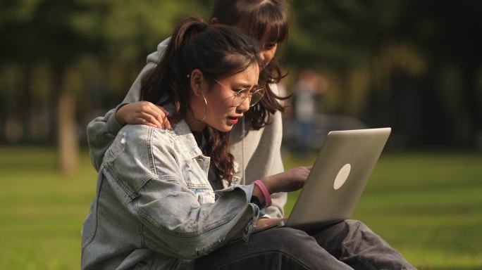 两位学生坐在大学校园草地上看书学习用电脑