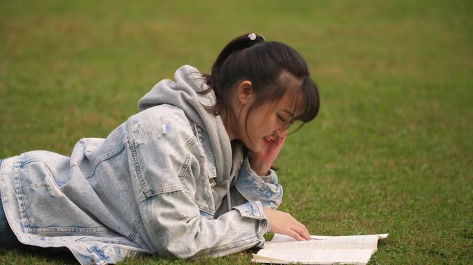 大学校园里女学生趴在草地上看书学习休闲