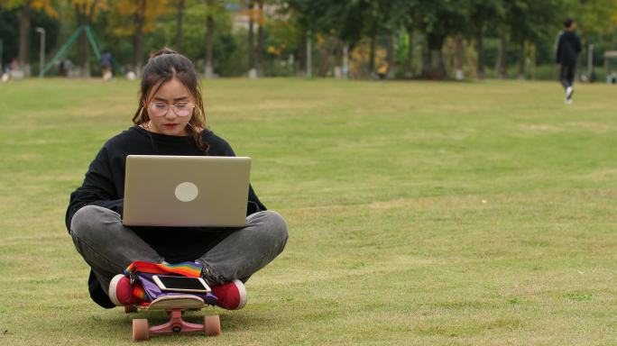 大学校园里女大学生坐在滑板上用电脑学习