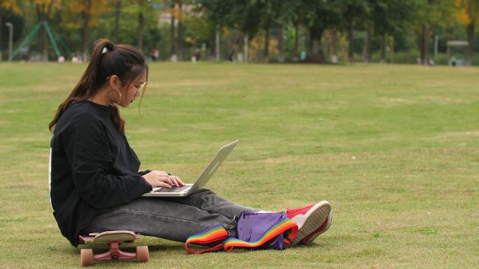 大学校园里女大学生坐在滑板上用电脑学习