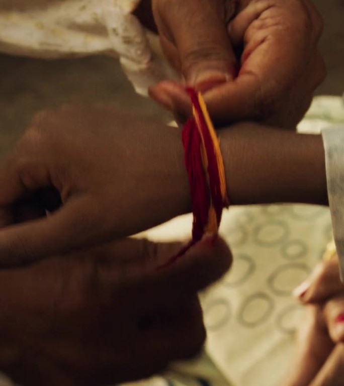 竖屏:印度祭司在寺庙里用毛利线系住男孩手腕的真实特写。小家庭拜访他们的高级导师，寻求指导。家族长者传