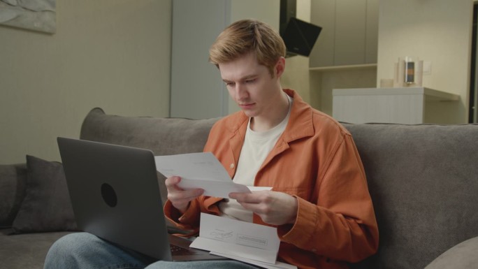 看着笔记本电脑处理文件的男人。30多岁的企业家，在家办公室管理文件、发票、税单。