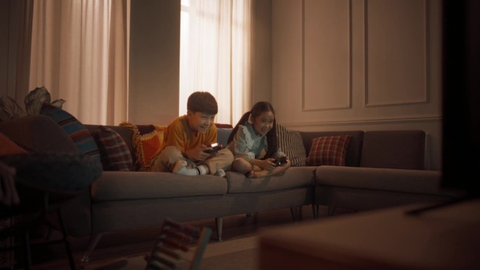 可爱的小兄妹在客厅沙发上的游戏机上玩电子游戏。韩国兄弟姐妹在比赛中获胜，庆祝并互相击掌。放学后玩得开