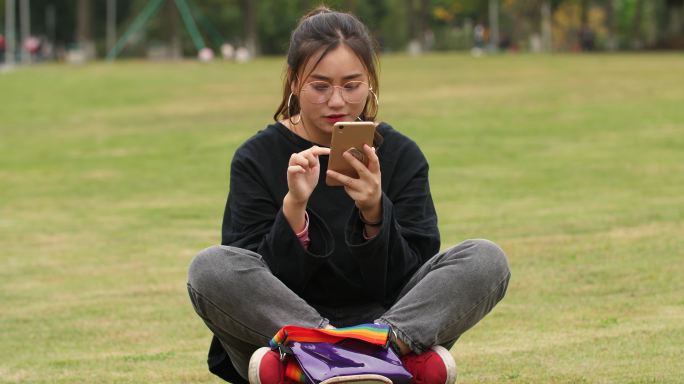 大学校园草地上女大学生坐在滑板上玩手机