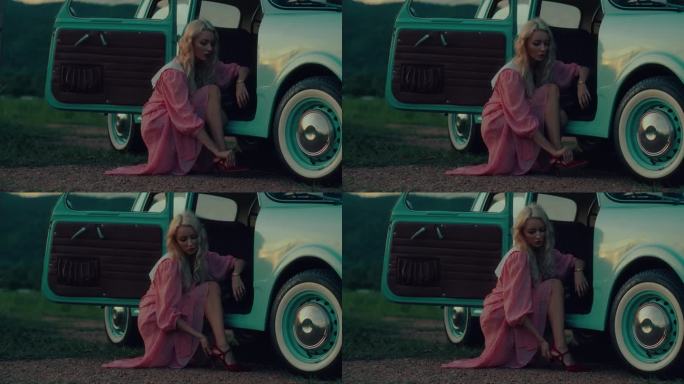 一个女孩的肖像，穿着粉红色的复古连衣裙，坐在一辆绿松石色的复古车旁边